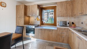 A compact kitchen with wooden cabinets, a built-in oven, a microwave, and a window overlooking a residential area.