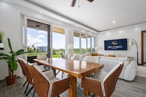 A modern hotel room with a dining area, a sofa set, a large window with a view, and a mounted sign.