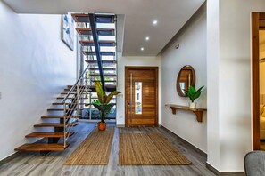 A modern interior with a wooden staircase, a potted plant, a wooden door, and a mirror on the wall. - Elite Living |Rooftop Sun| Kite Beach|Heated Jacuzzi Pool (Cabarete)