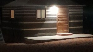 Una cabaña de troncos con un porche, una ventana pequeña y una puerta.