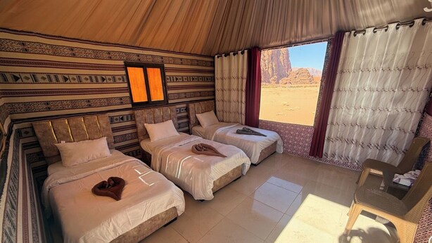 Una habitación con tres camas, una mesita y vista al desierto.