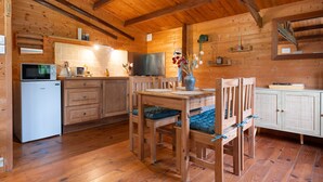 Een houten cabin met een eettafel, stoelen, een magnetron, kastjes en een televisie.