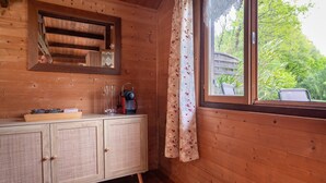 Een houten hut van binnen, met een houten kast, een radio en een raam met gordijn.