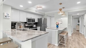 Uma cozinha moderna com armários brancos, eletrodomésticos de aço inoxidável e uma ilha de mármore com banquetas.