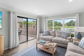 Ein Wohnzimmer mit Sofa, Couchtisch und Blick auf einen See und Bäume.
