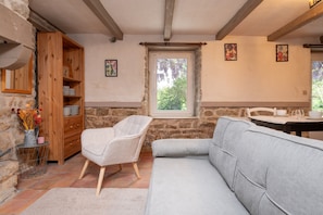 Una camera accogliente con parete in pietra, un mobiletto in legno, un divano imbottito, un tavolino con un vaso e una finestra vista.