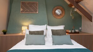 Une chambre à coucher avec un lit, des oreillers, une table de chevet avec une lampe, un miroir et une plante suspendue.