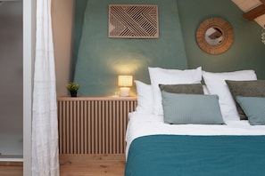 Una camera da letto con un letto, cuscini, un comodino con una lampada, una decorazione a parete e un pannello in legno.