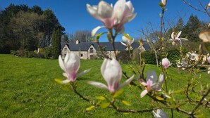 Un bâtiment en pierre à l’architecture traditionnelle, entouré d’une pelouse bien entretenue et d’arbres.