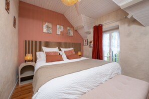 Un dormitorio con techo inclinado, cama con cabecera a rayas, lámpara de noche y cuadros en la pared.
