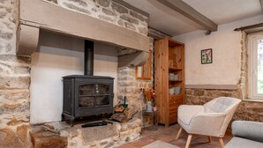 A stone fireplace with a black stove, a wooden cabinet, a chair, and a window. - Guesthouse “Lorient Room” with Terrace and Shared Garden (Guilligomarc'h)