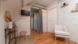 A room with wooden flooring, a white chair, a television mounted on the wall, and a door leading to another room. - Guesthouse “Lorient Room” with Terrace and Shared Garden (Guilligomarc'h)