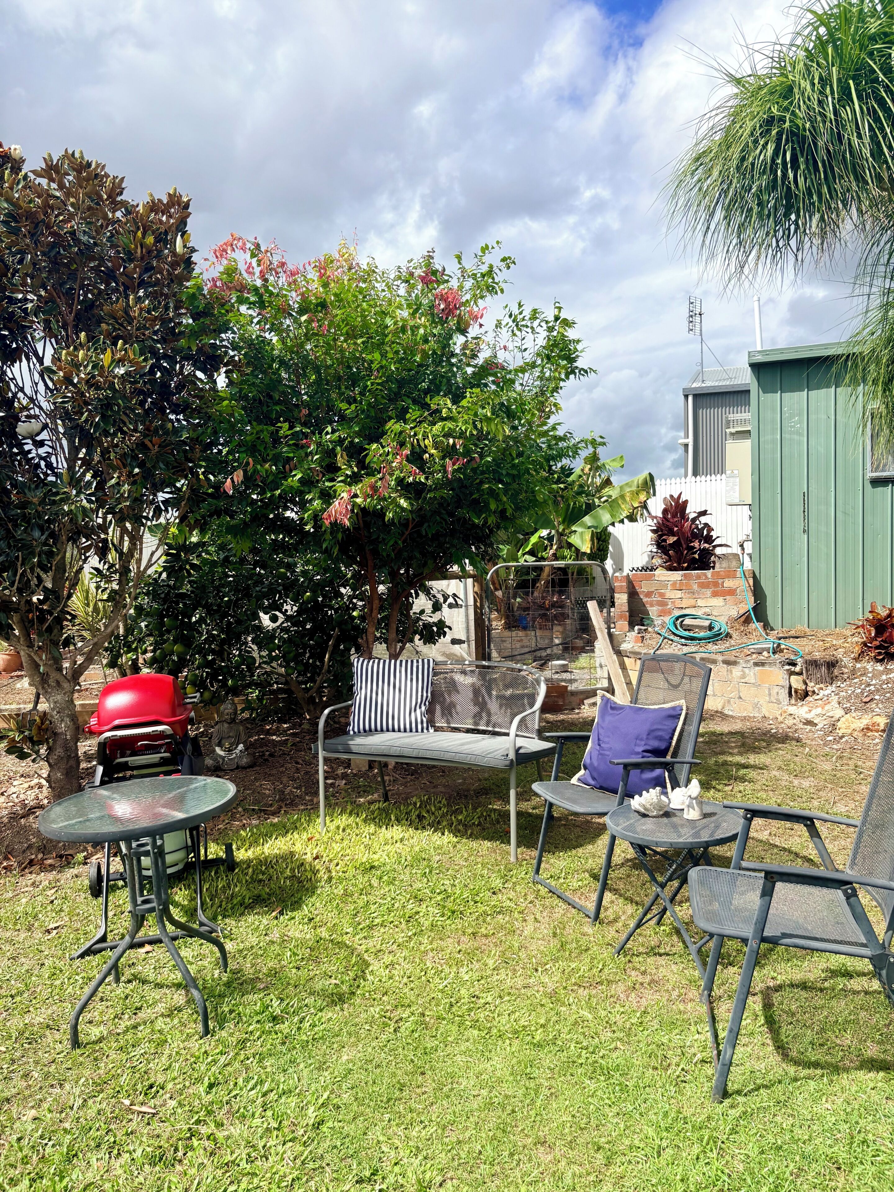 A backyard with a barbecue grill, outdoor seating, and a green shed.