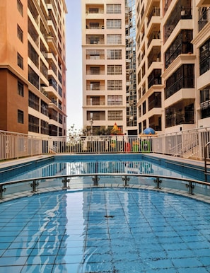 A swimming pool surrounded by high-rise buildings with balconies. - Luxurious 4-bedroom Apartment With Pool Access in Lavington (Nairobi)