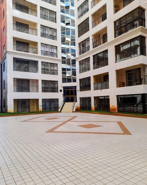 A multi-story building with a central staircase leading to the entrance, surrounded by a tiled courtyard. - Luxurious 4-bedroom Apartment With Pool Access in Lavington (Nairobi)