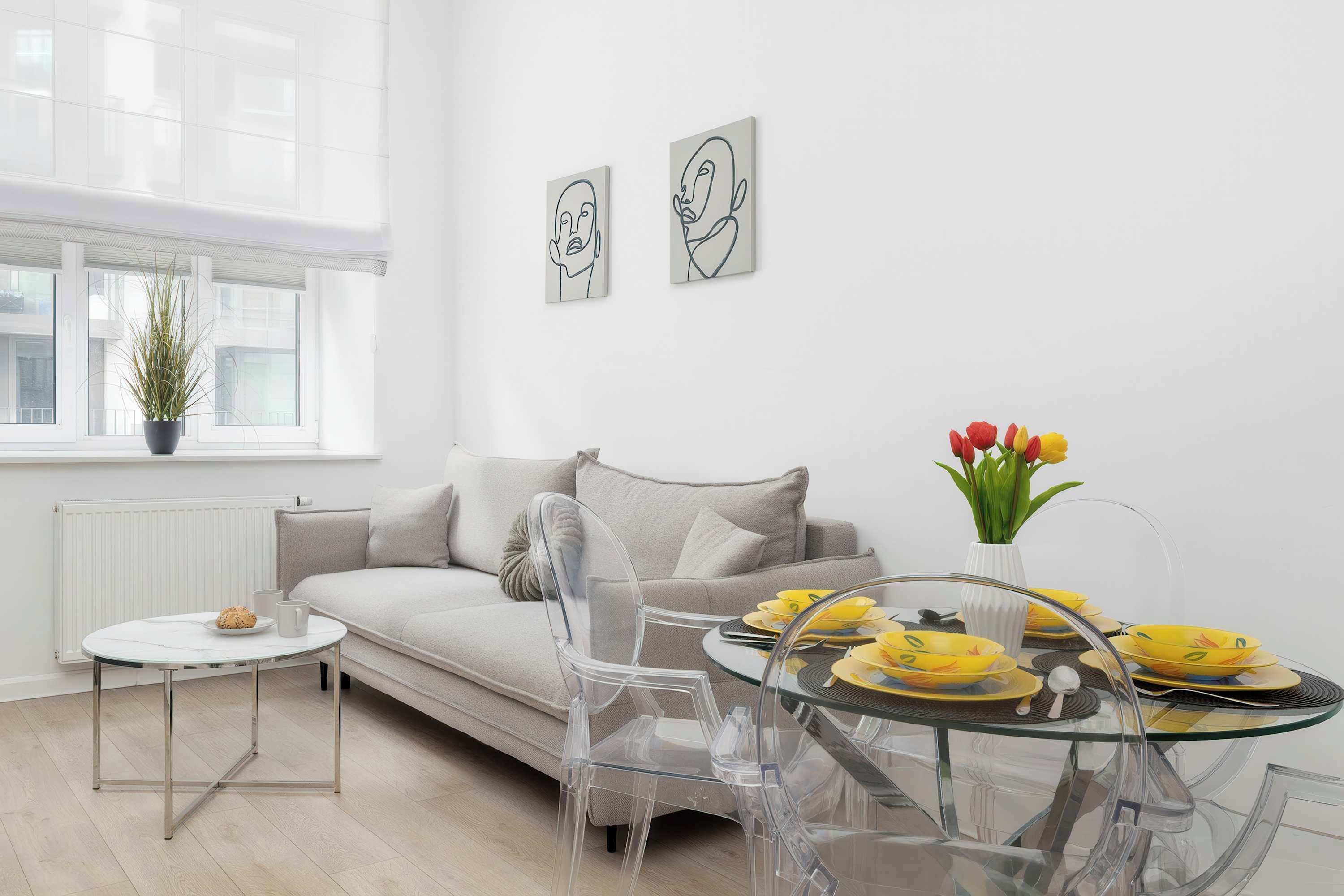 A modern living room with a sofa, clear chairs, a glass table, and artwork on the wall.