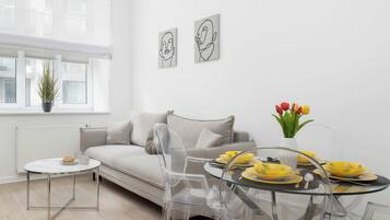 A modern living room with a sofa, clear chairs, a glass table, and artwork on the wall.