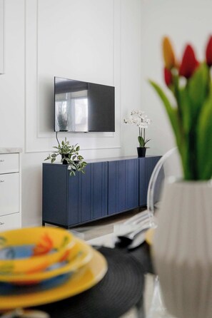 Ein modernes Wohnzimmer mit einem an der Wand befestigten Flachbildfernseher, einem dunkelblauen Schrank und einer Topfpflanze.