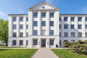Ein mehrstöckiges Gebäude mit einer symmetrischen Fassade, großen Fenstern und einem zentralen Eingang.
