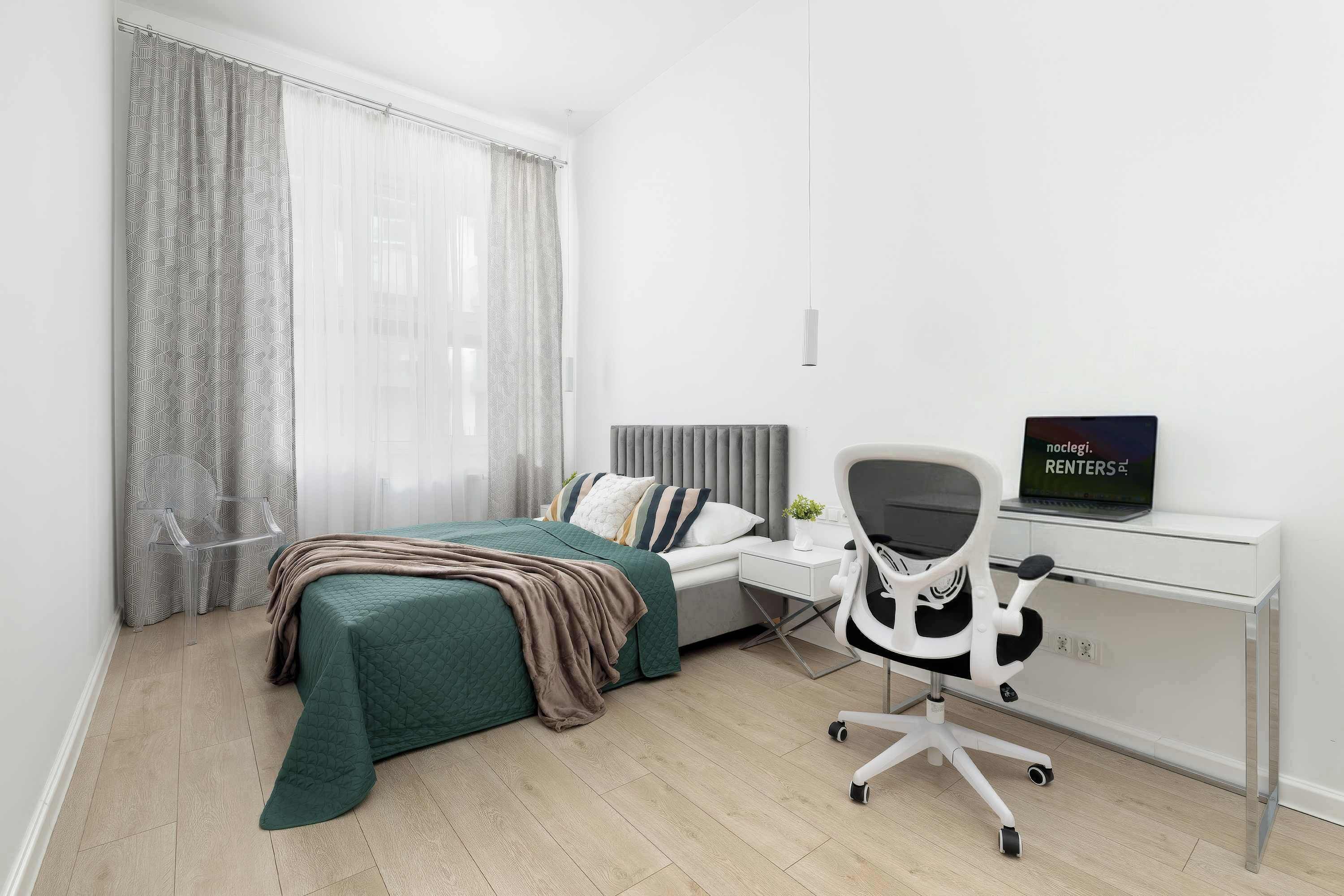 Un dormitorio moderno con una cama, un escritorio, una silla y una computadora portátil.