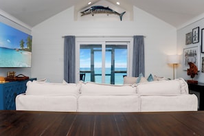 Ein Wohnzimmer mit einem weißen Sofa, Holzboden, einem großen Fenster mit Meerblick und einer Hai-Dekoration an der Decke.