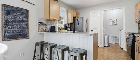 A kitchen with a chalkboard, wooden cabinets, a refrigerator, and three bar stools.