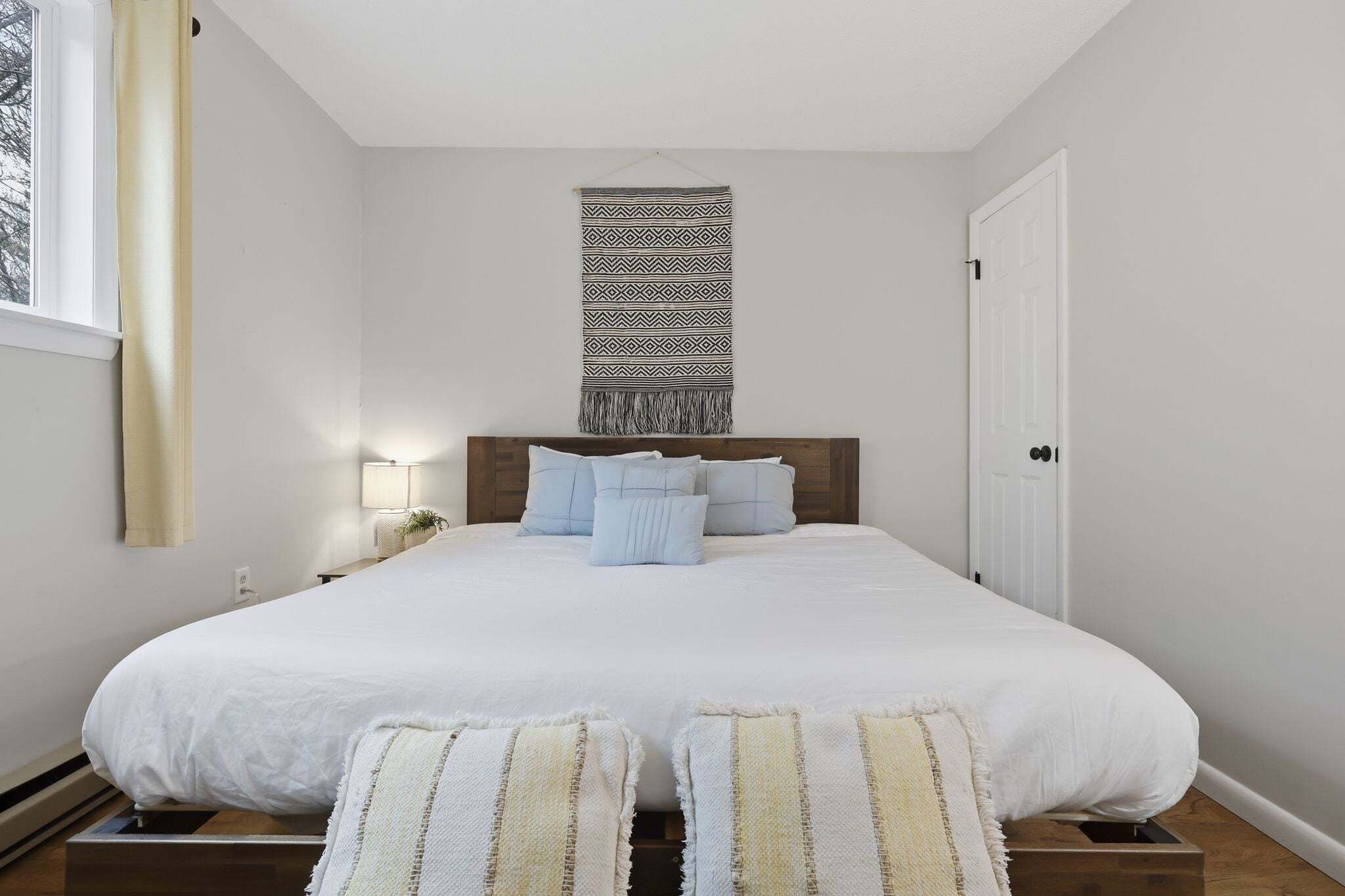 A bedroom with a large bed, a headboard, bedside lamps, and a window with curtains.