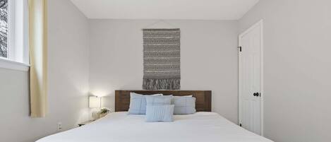 A bedroom with a large bed, a headboard, bedside lamps, and a window with curtains.
