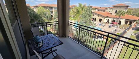 A balcony with a table and chairs, overlooking a courtyard with buildings and greenery.