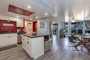 A modern kitchen with white cabinets, a granite countertop, and a dining area with a round table and chairs. - Maui Banyan P202 2 Bedroom Condo (Kihei)