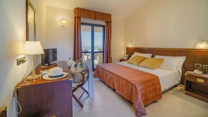 A hotel room with a bed, a desk with a lamp, a television, and a view of the outdoors. - FRUIT VILLAGE BAIA DELLA ROCCHETTA (Briatico)