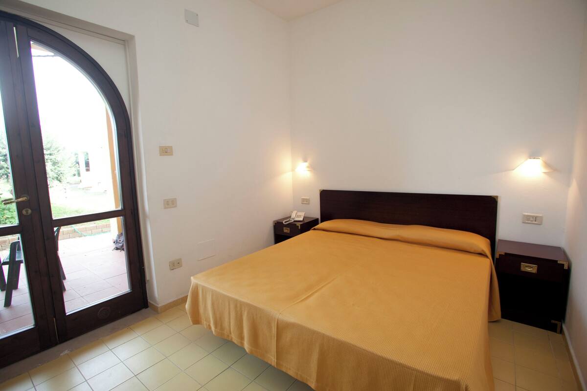 Un dormitorio con cama, mesita de noche, teléfono y puerta que da a un espacio exterior.