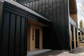 Un bâtiment moderne à l’extérieur sombre, doté d’une porte en bois et d’un numéro de maison bien visible.