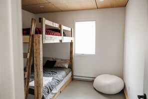 Un lit superposé avec une fenêtre, un pouf rond et une porte.