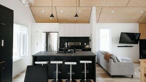 Une cuisine moderne avec un îlot central, des tabourets de bar, un canapé gris, un téléviseur à écran plat et un plafond en bois.