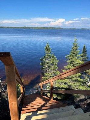 Una escalera de madera que conduce a un muelle con vistas a un lago tranquilo y árboles.