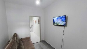 A room with a sofa, a television mounted on the wall, and a door leading to another room. - Hostel Vila Univesitária (Bauru)
