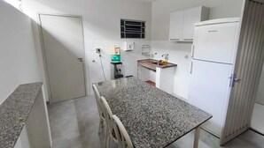 A compact kitchen with a granite countertop, white cabinets, a refrigerator, and a water dispenser. - Hostel Vila Univesitária (Bauru)