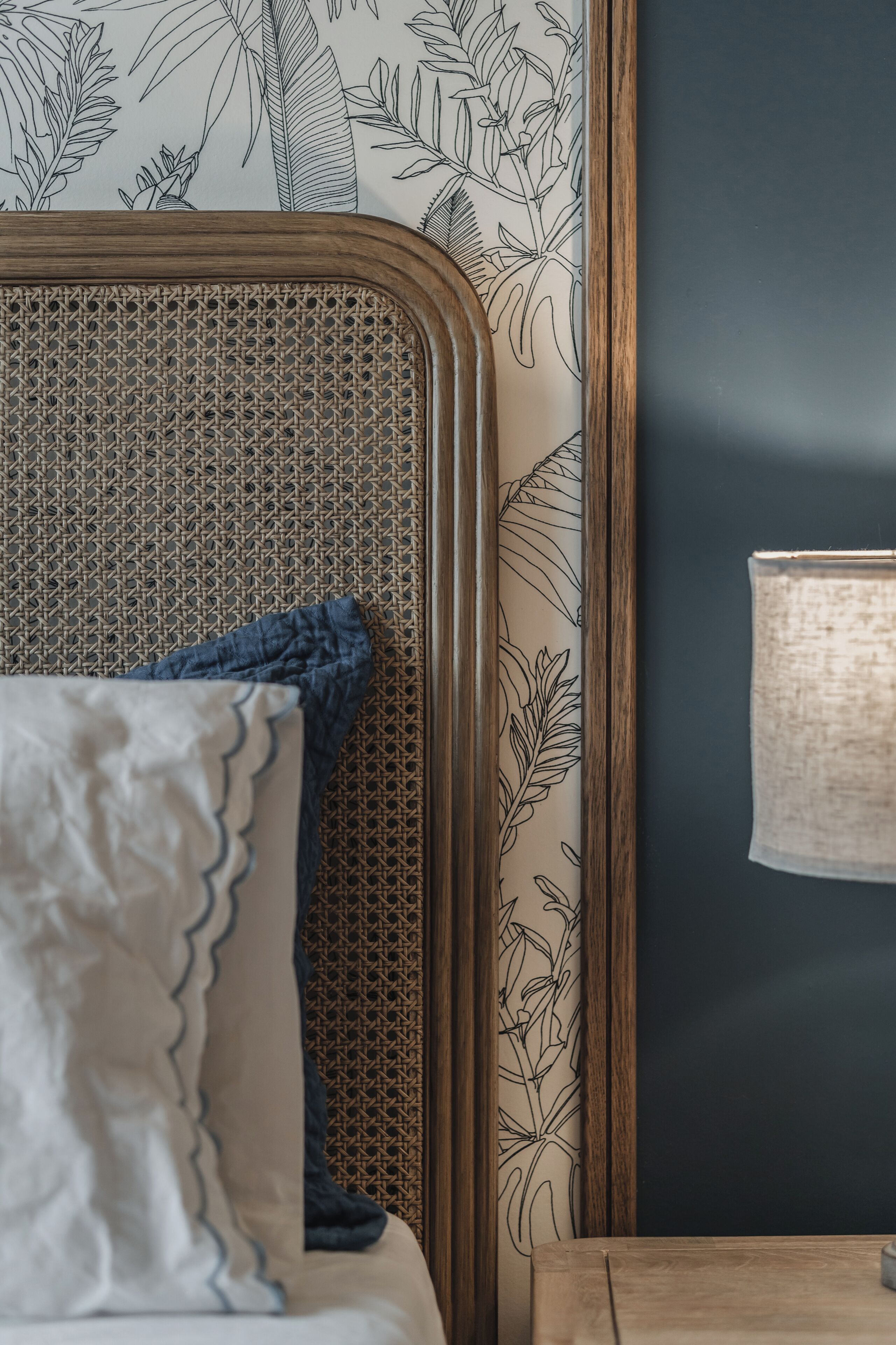 A bed with a rattan headboard, a blue pillow, and a white pillow with a scalloped edge.