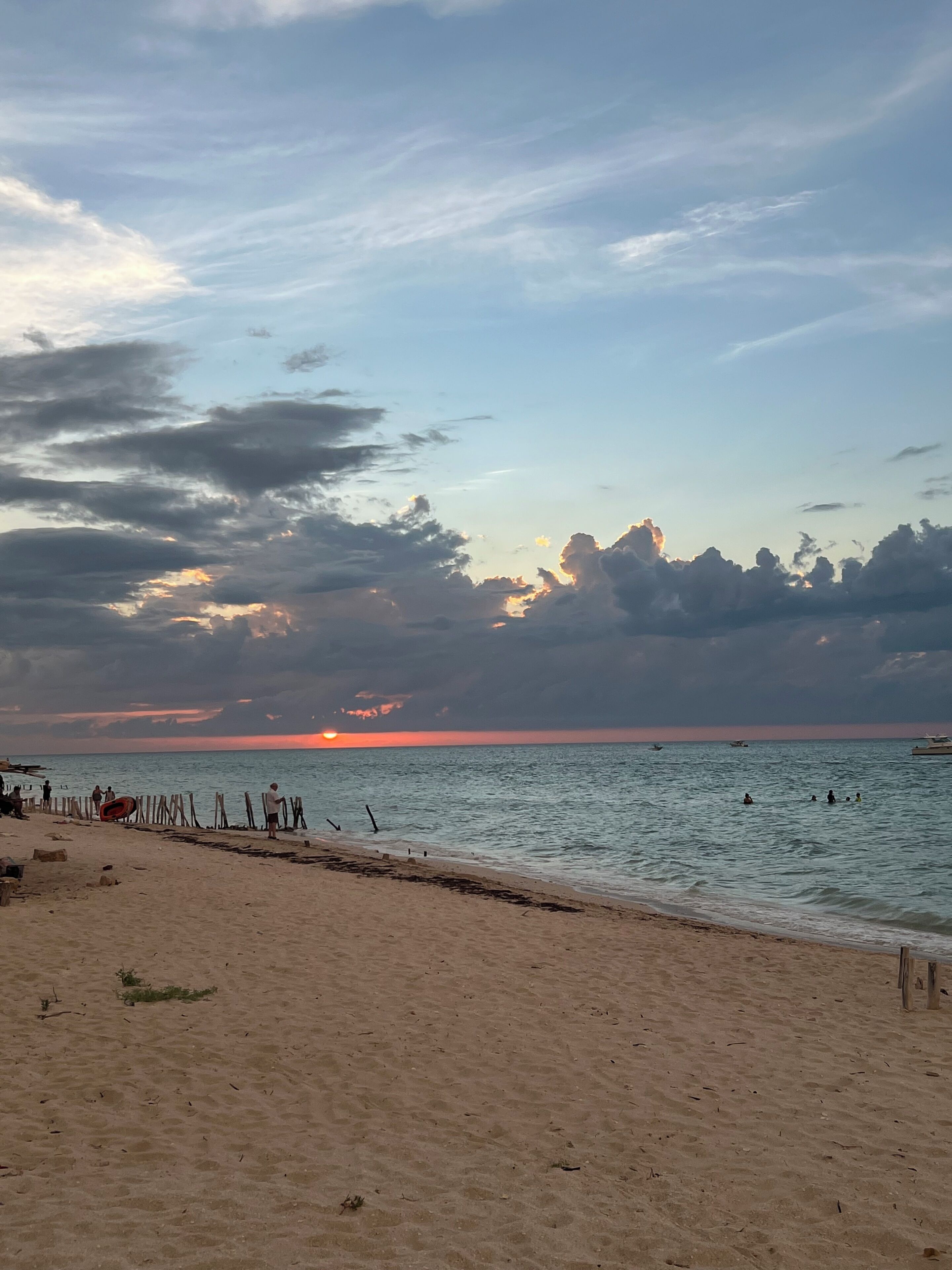 A beach with a wooden fence, calm sea, and a sunset.