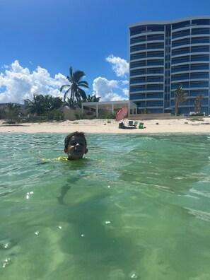 A child swimming in clear water with a beach and a hotel in the background. - A place of peace in front of the sea (Chelem)