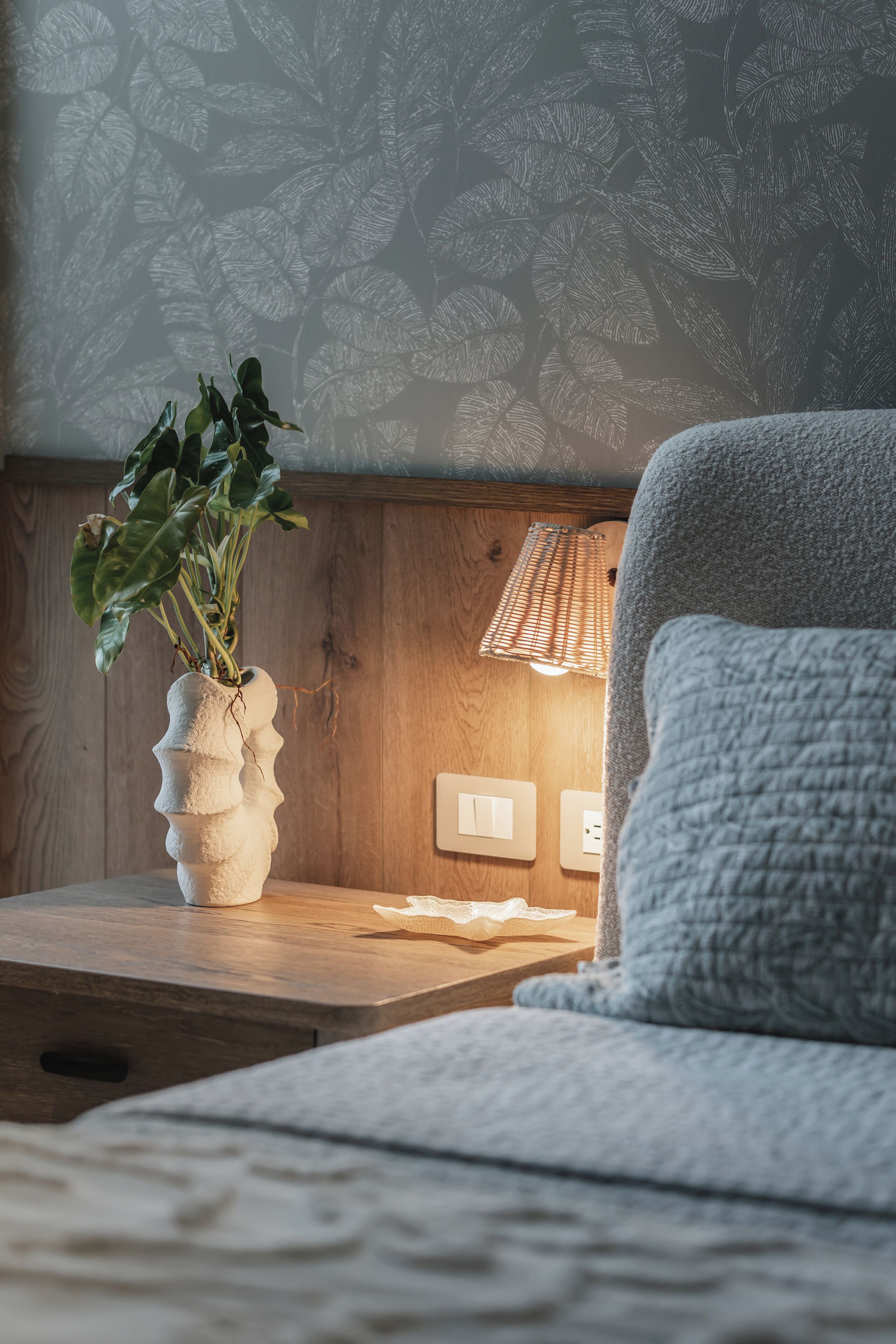 Une chambre avec une table de chevet en bois, un mur à texture, une lampe et un fauteuil confortable.