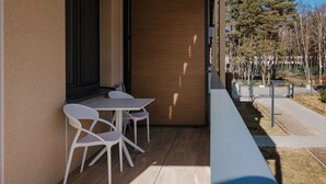 A modern outdoor seating area with a table and two chairs, a wooden wall, and a view of a park with trees and a fence. - Apartamenty Sun&Snow Aquamarina Dąbki (Dąbki)