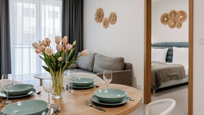 A dining area with a round table set with plates, glasses, and cutlery. There is a vase with flowers on the table. - Apartamenty Sun&Snow Aquamarina Dąbki (Dąbki)