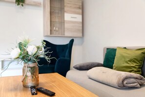 A wooden table with a vase of flowers, a remote control, and a sofa with green and gray cushions. - Apartment “Linke Hof” with Wi-Fi (Bobritzsch-Hilbersdorf)