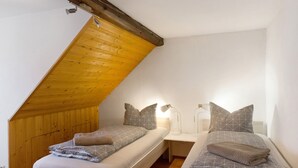 A bedroom with two beds, wooden ceiling beams, white walls, and bedside lamps. - Apartment “Linke Hof” with Wi-Fi (Bobritzsch-Hilbersdorf)
