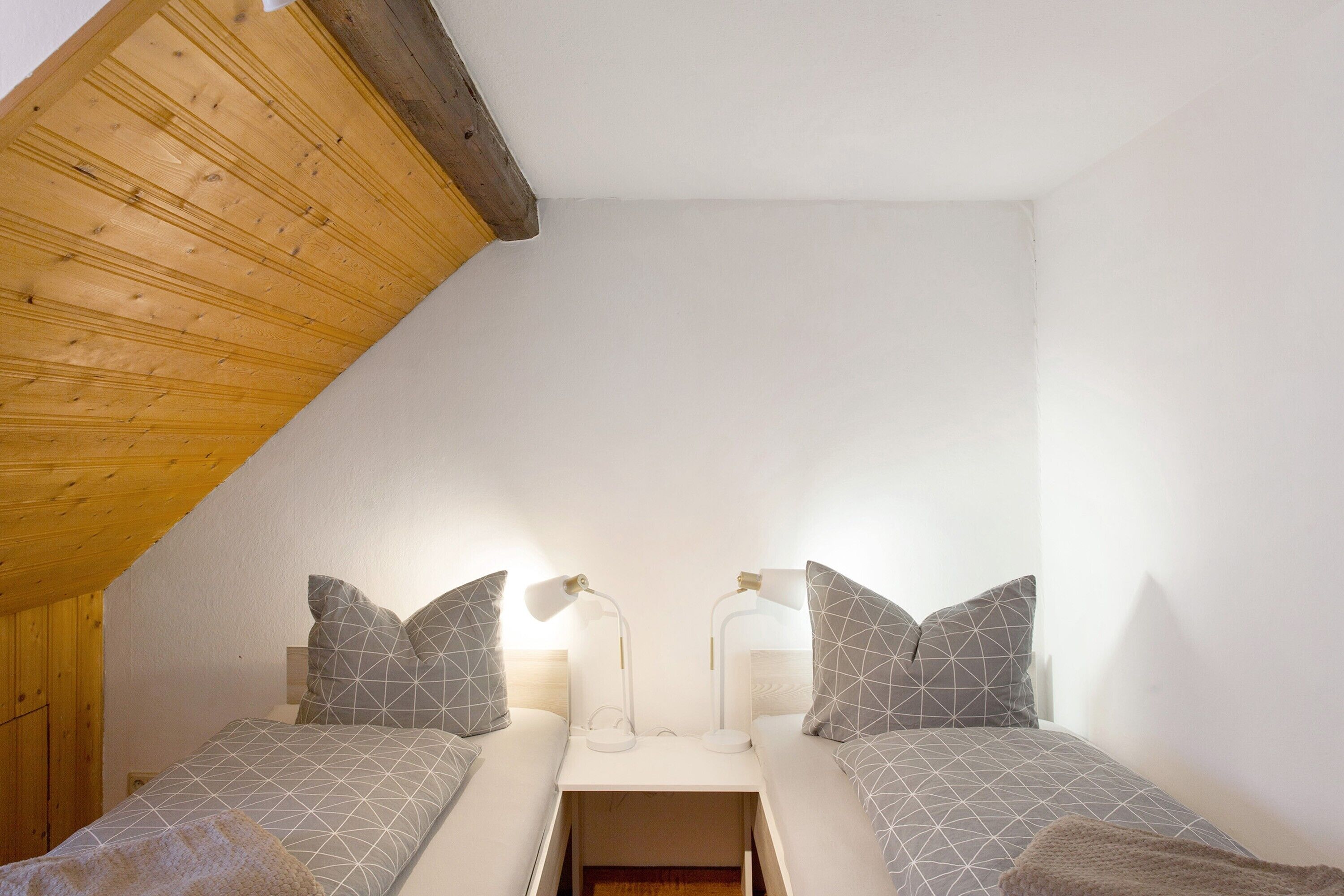 A small, cozy bedroom with two beds, wooden ceiling beams, and bedside lamps.