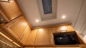 A compact kitchen with wooden cabinets, a microwave, and under-cabinet lighting. - Marylebone High Ceiling Private Spacious W1 Home - Luxurylondonstays (London)