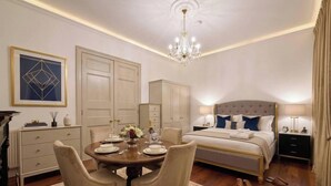 A bedroom with a bed, bedside tables, a chandelier, a dining area with chairs and a table, and a decorative wall piece. - Marylebone High Ceiling Private Spacious W1 Home - Luxurylondonstays (London)