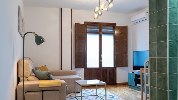 Una sala de estar con sofá, una mesa de centro, una lámpara, televisor y un ventanal con contraventanas de madera.